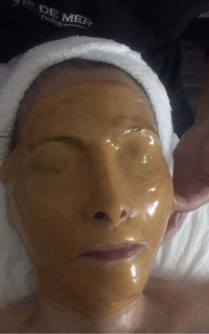 Person with a gold facial mask on their face, wrapped in a towel.
